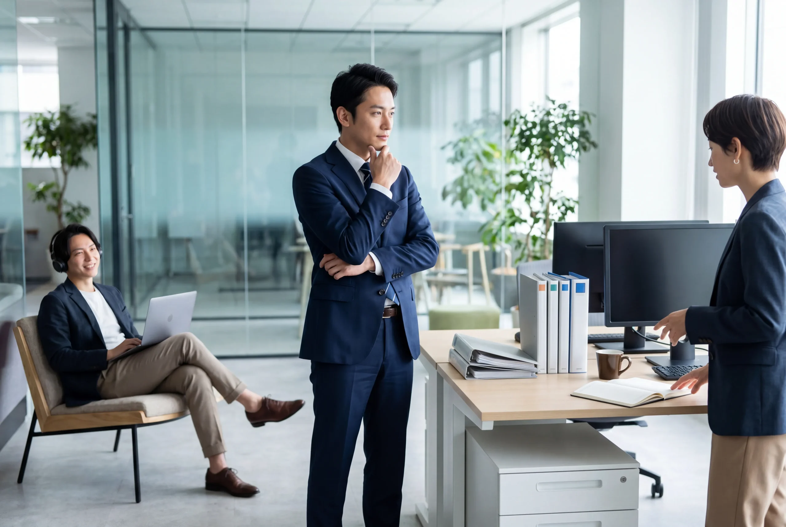 Homme en costume réfléchissant lors d’une discussion professionnelle dans un bureau moderne avec deux collègues