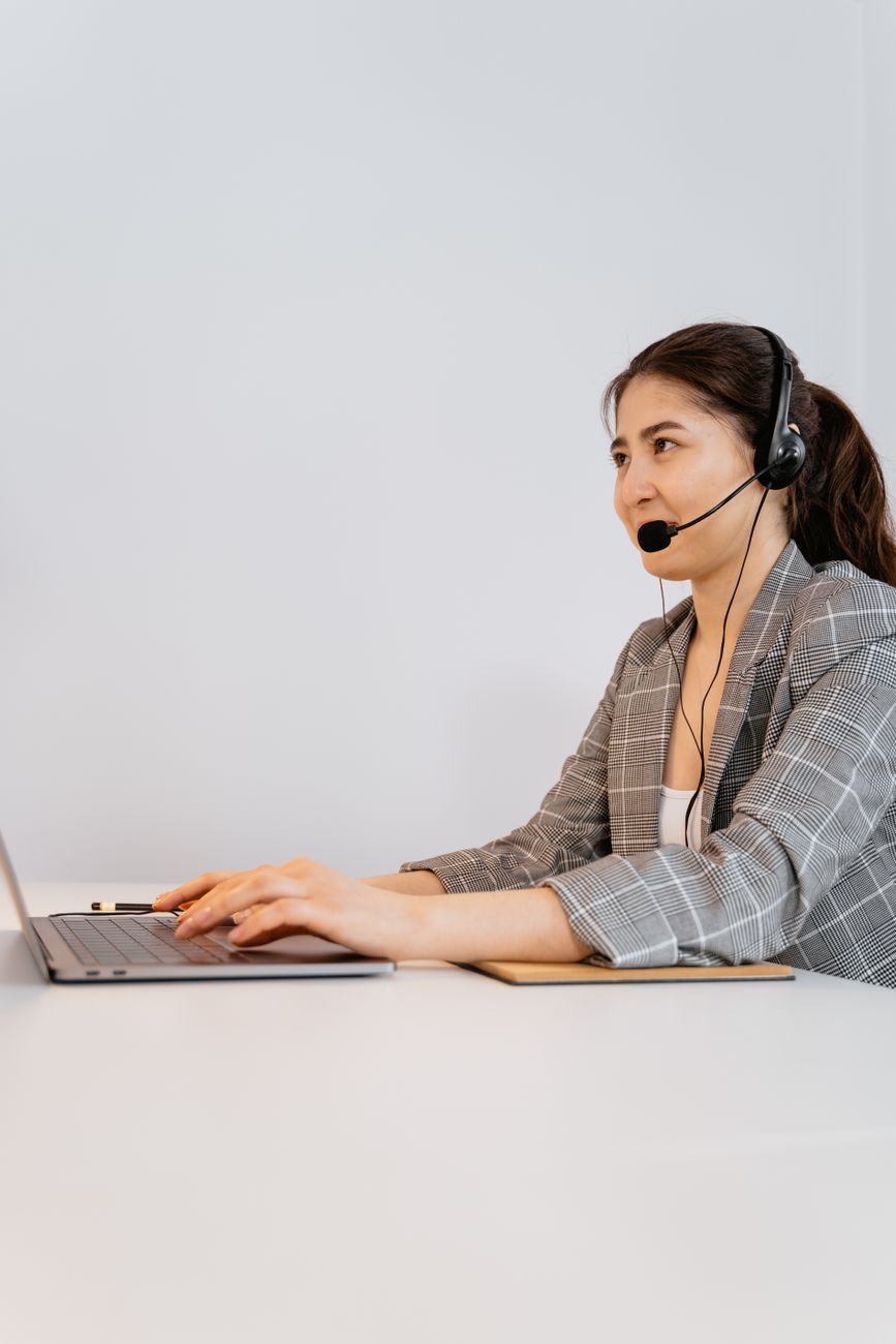 Femme professionnelle en blazer à carreaux utilisant un ordinateur portable avec un casque dans un cadre de bureau.